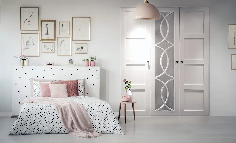 A creme walled bedroom with a white wardrobe fitted into the wall with mirrors on the doors, there is a bed with several pictures hanging above it
