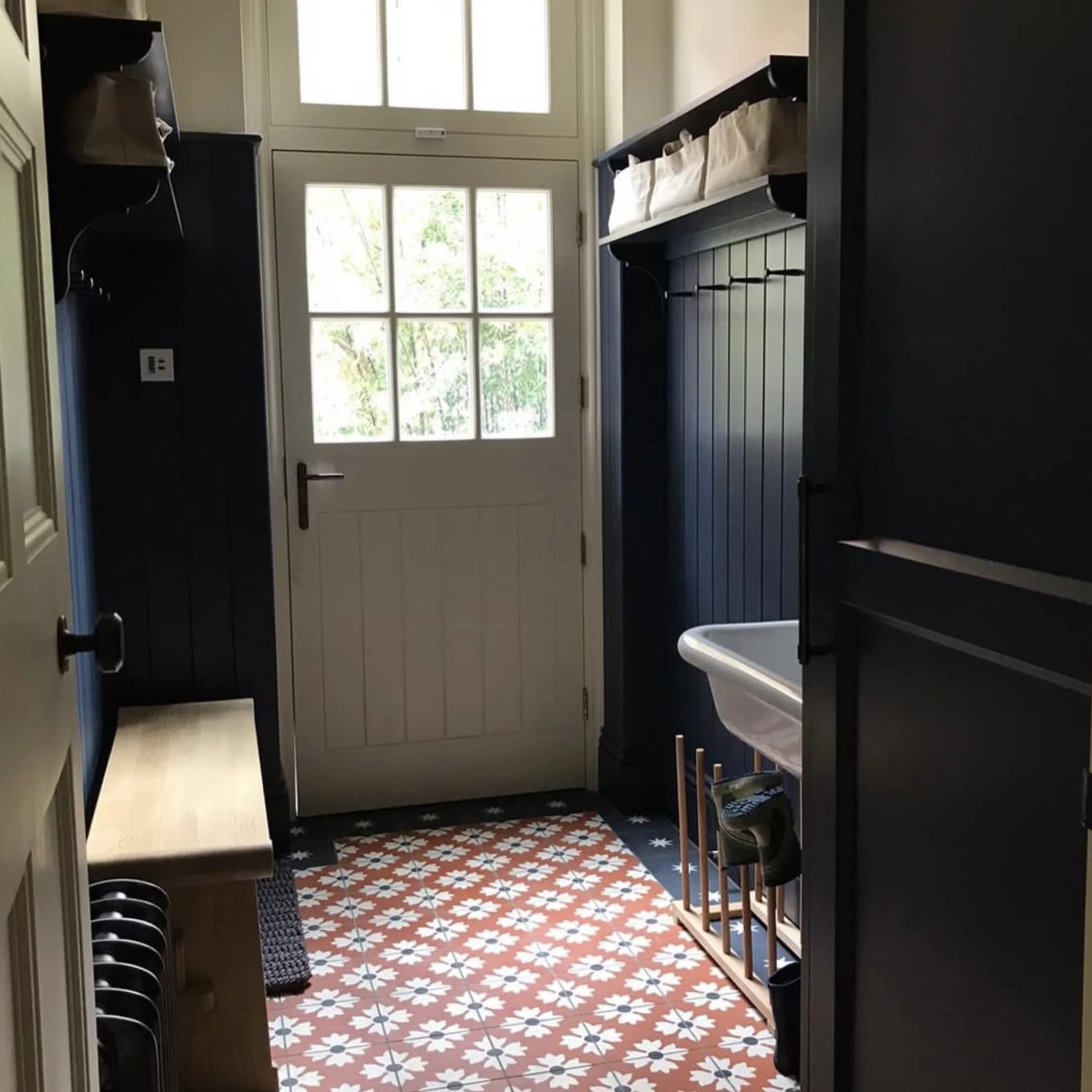 A bespoke boot room with dark blue paneling, built-in storage and patterned floor tiles