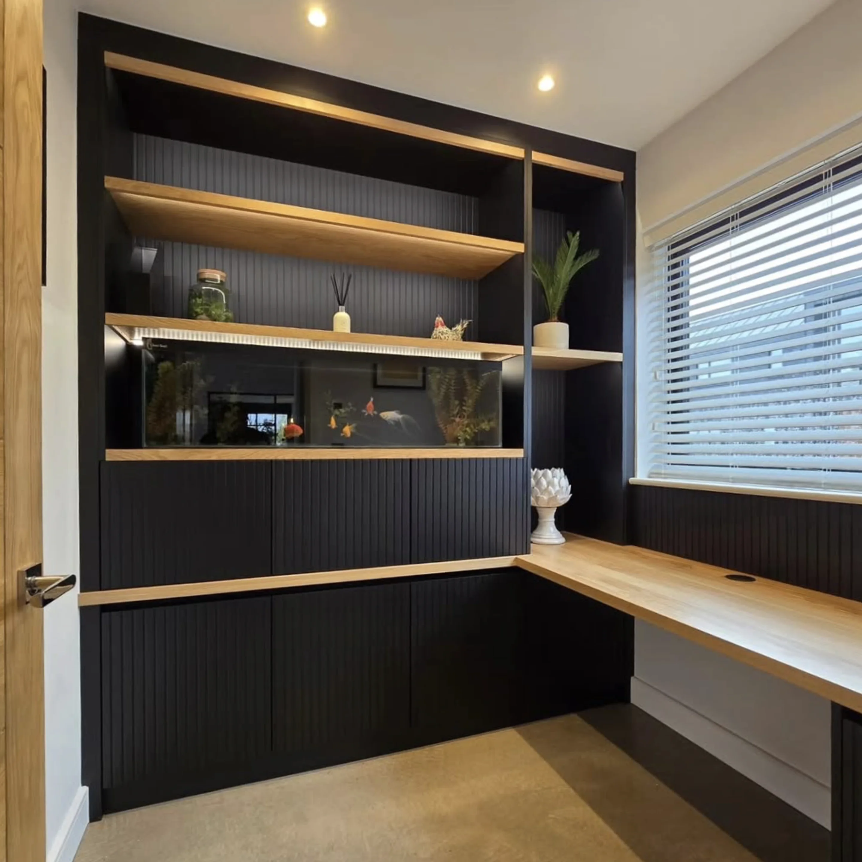 A fitted home office with dark fluted shelving unit, integrated fish tank and oak desk
