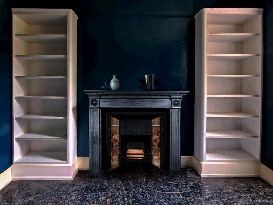 A victorian style room with a fireplace and large white book cases either side