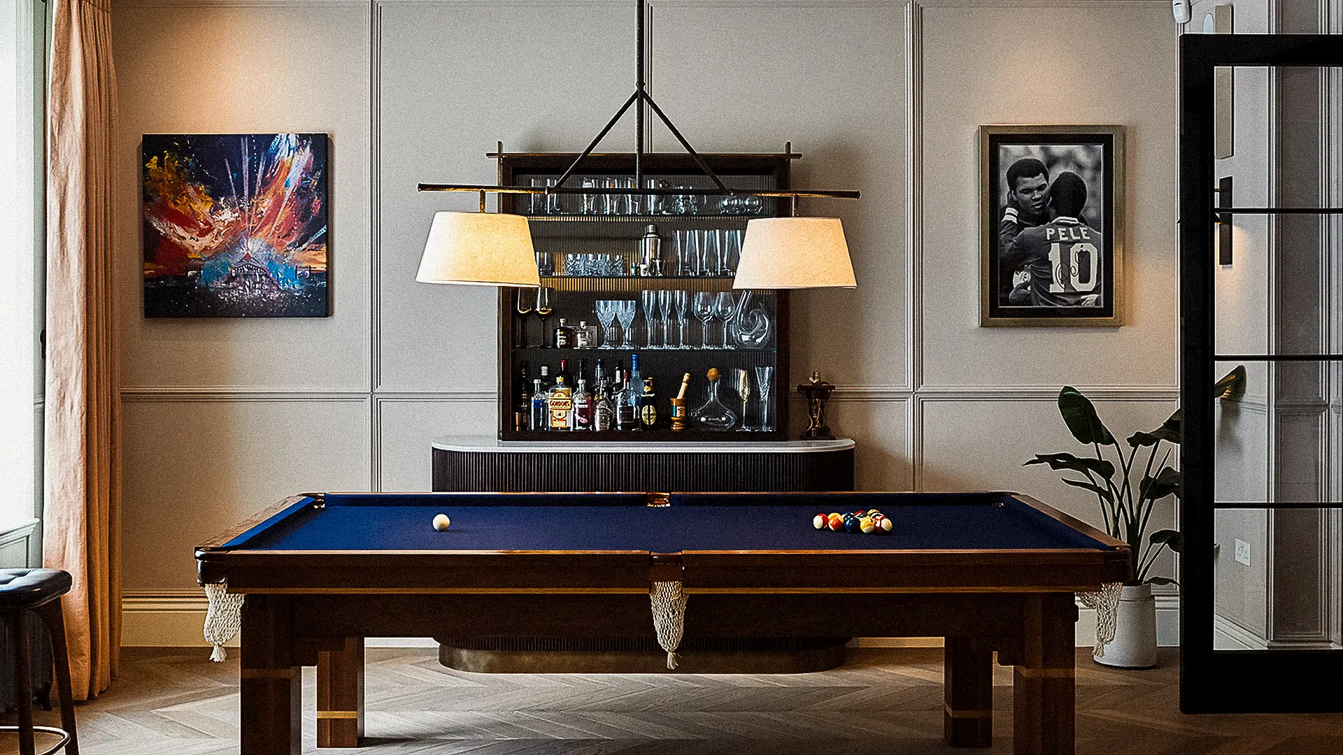 A games room with a pool table and dark wooden bar with a selection of drinks and glassware