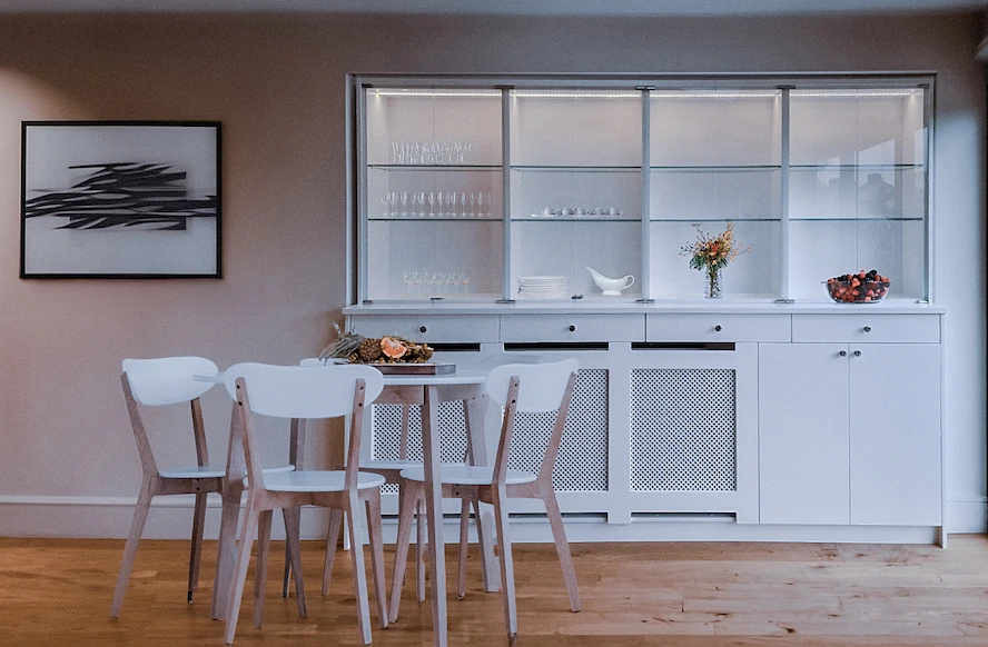 A White themed dining area with a table and chairs and a large white storage unit recessed into the wall