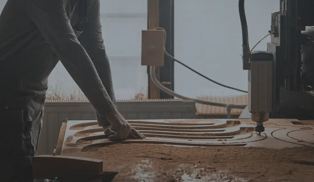 A man leans over a CNC machine thats cutting a design into wood