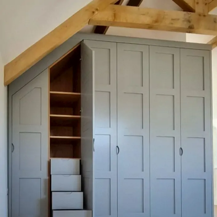 A green wardrobe in a room with wooden beams, the wardrobe drawers are open to show ample space