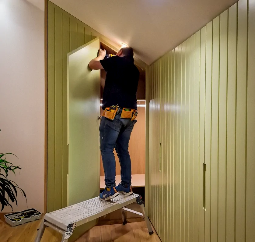A Man in grey overalls installing a wardrobe