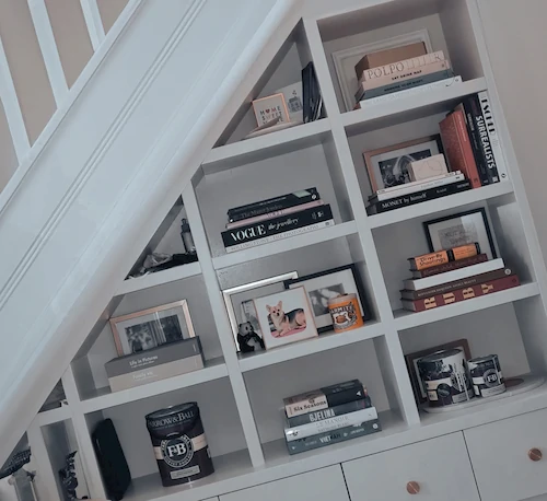 White shelving fitted underneath a staircase, various books and family pictures placed on the shelves