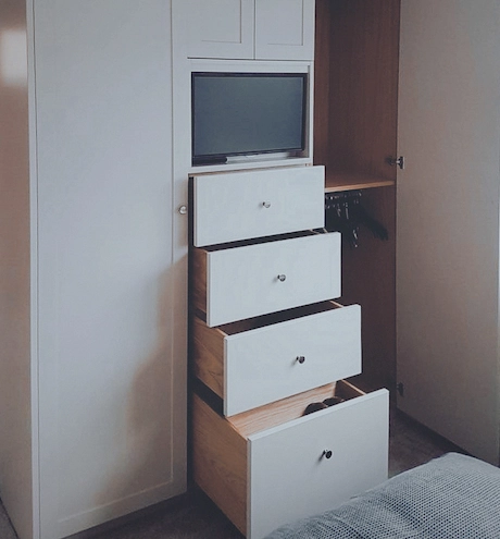 A White fitted wardrobe with its drawers open to show lots of space, there is a TV Built into the upper part of the wardrobe